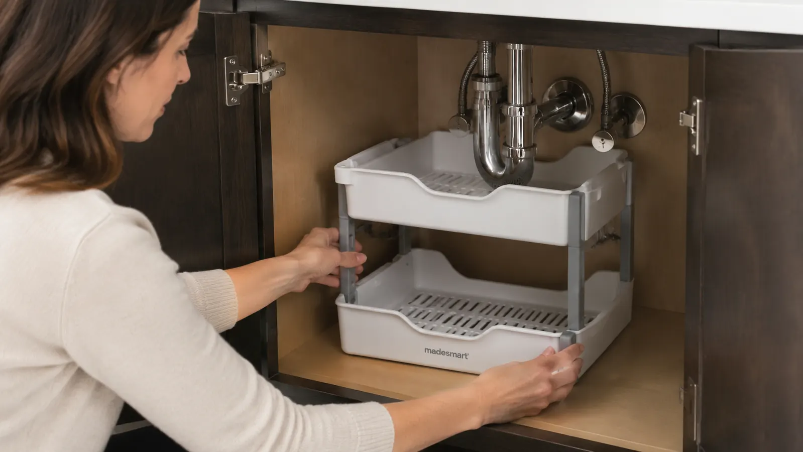 Hand pulling out the lower sliding drawer of a madesmart 2-tier under-sink organizer loaded with cleaning bottles