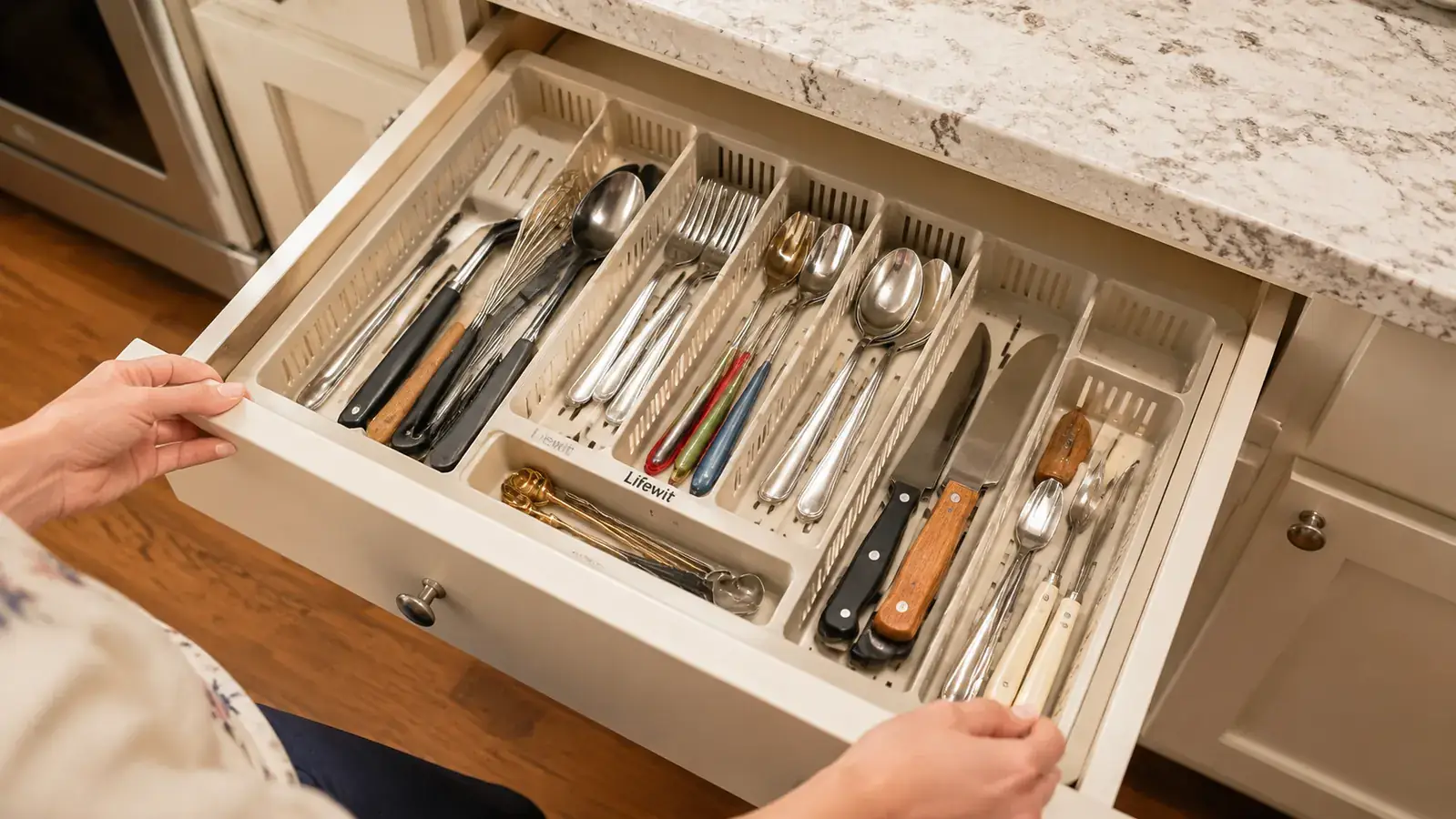 Hand placing a wooden spatula into a large slot of the Lifewit expandable drawer organizer inside a kitchen drawer